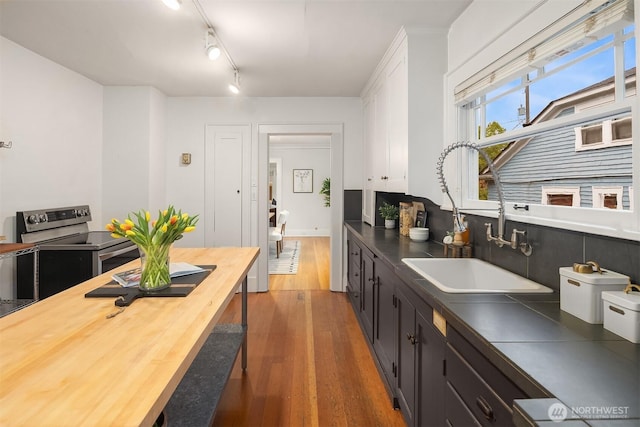 kitchen with wooden counters, stainless steel electric range oven, wood finished floors, a sink, and white cabinets