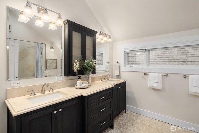 bathroom featuring a sink, baseboards, double vanity, and lofted ceiling