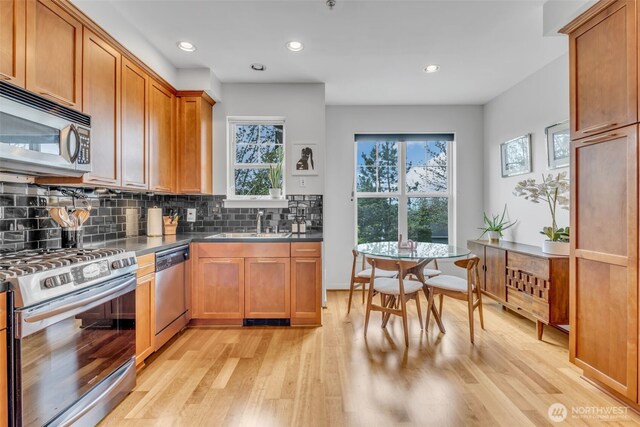 kitchen with light wood-type flooring, appliances with stainless steel finishes, backsplash, and brown cabinets
