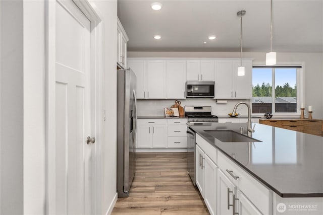 kitchen featuring dark countertops, appliances with stainless steel finishes, a sink, white cabinetry, and light wood-type flooring