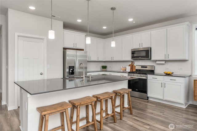 kitchen with dark countertops, appliances with stainless steel finishes, light wood-style flooring, and a sink