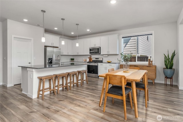 kitchen featuring a breakfast bar, dark countertops, a center island with sink, white cabinetry, and stainless steel appliances