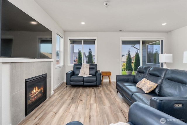 living room featuring a tiled fireplace, recessed lighting, light wood-style flooring, and baseboards