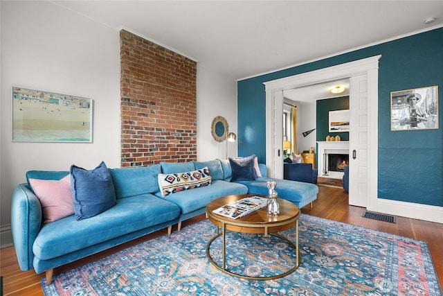 living room with baseboards, a warm lit fireplace, visible vents, and wood finished floors