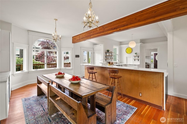 dining room featuring beamed ceiling, a chandelier, baseboards, and light wood-style floors
