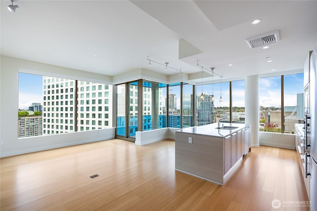 kitchen with light wood finished floors, a view of city, a kitchen island, visible vents, and modern cabinets