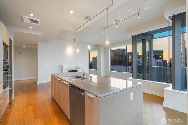kitchen featuring appliances with stainless steel finishes, a sink, an island with sink, visible vents, and modern cabinets
