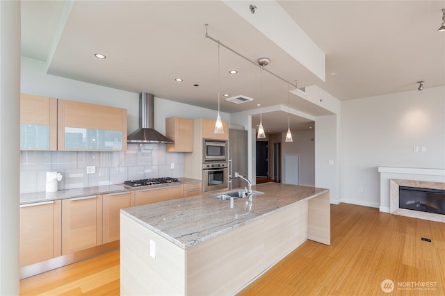 kitchen with light wood-style floors, wall chimney exhaust hood, light brown cabinets, and stainless steel appliances