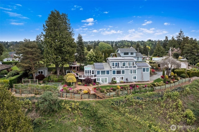 rear view of house with a fenced backyard, a patio, roof mounted solar panels, and a wooded view