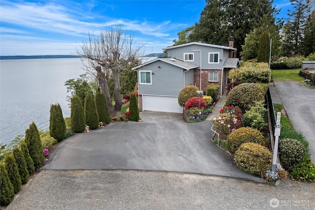 view of front of property featuring an attached garage, brick siding, a water view, a chimney, and driveway