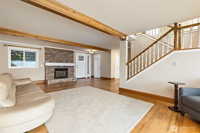 living room with stairs, a brick fireplace, wood finished floors, beamed ceiling, and baseboards