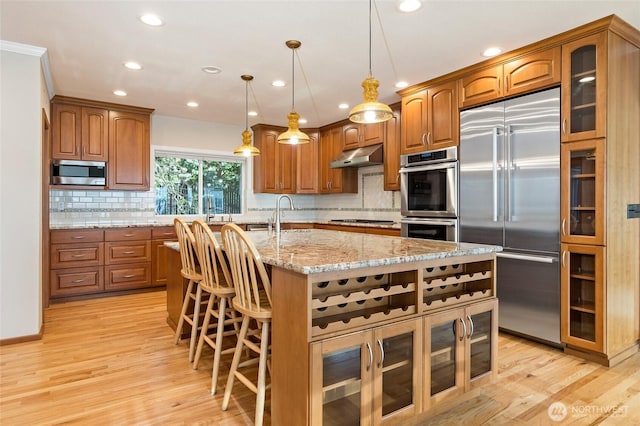kitchen with brown cabinetry, under cabinet range hood, and stainless steel appliances