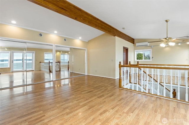 unfurnished room featuring wood finished floors, beamed ceiling, baseboards, ceiling fan, and a wall unit AC