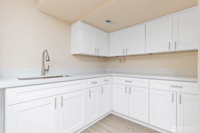 kitchen with a sink, white cabinetry, light wood-style flooring, and light countertops