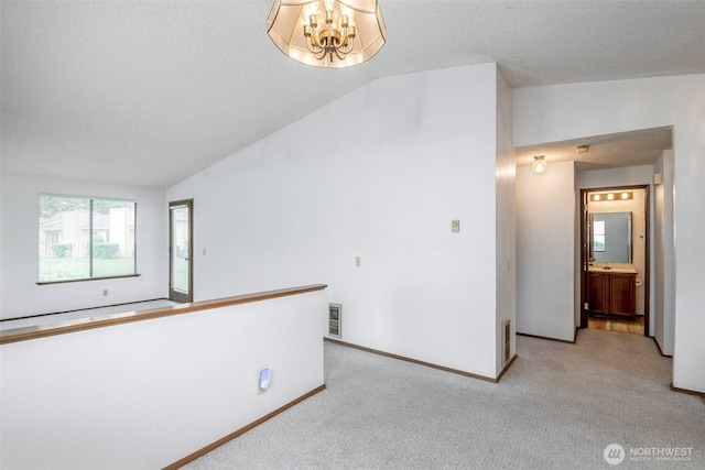 carpeted spare room with visible vents, a textured ceiling, a notable chandelier, and lofted ceiling