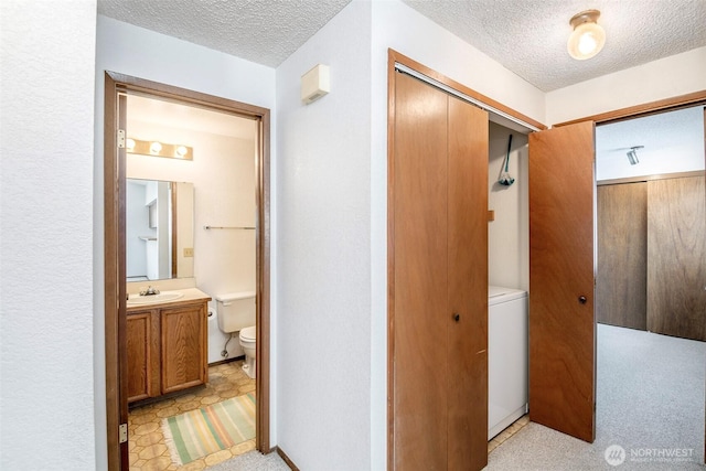 hallway with light floors, a sink, a textured ceiling, and washer / dryer