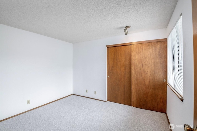unfurnished bedroom with carpet flooring, a textured ceiling, baseboards, and a closet