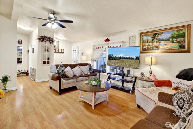 living area with a ceiling fan, light wood-style flooring, baseboards, and vaulted ceiling