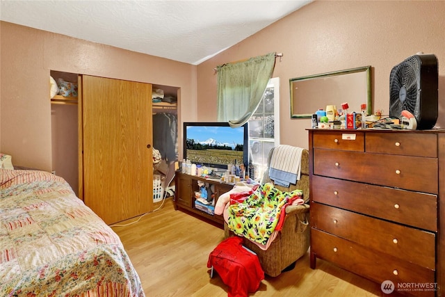 bedroom with wood finished floors, vaulted ceiling, a closet, and a textured wall