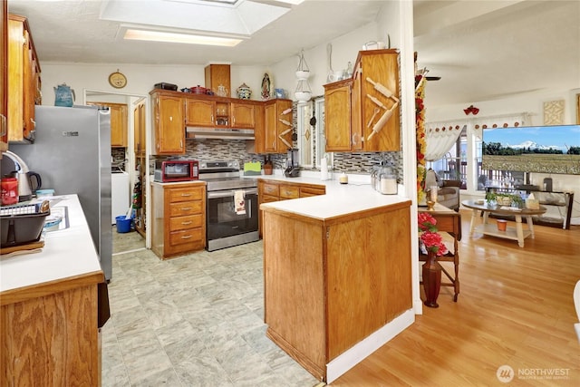 kitchen featuring stainless steel appliances, a peninsula, tasteful backsplash, under cabinet range hood, and light countertops