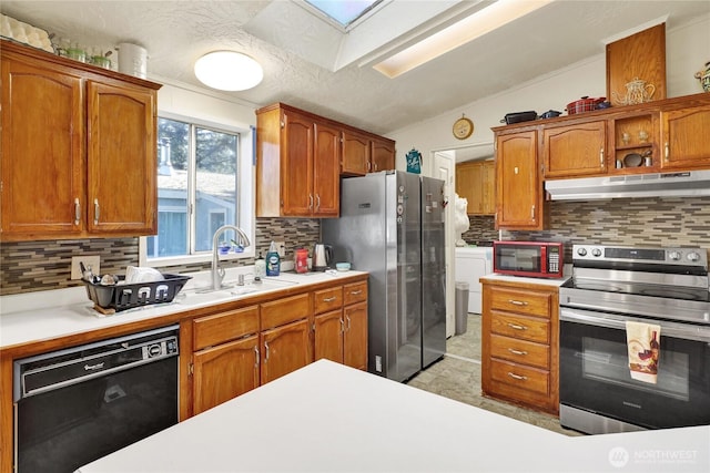 kitchen featuring appliances with stainless steel finishes, under cabinet range hood, a sink, tasteful backsplash, and a skylight