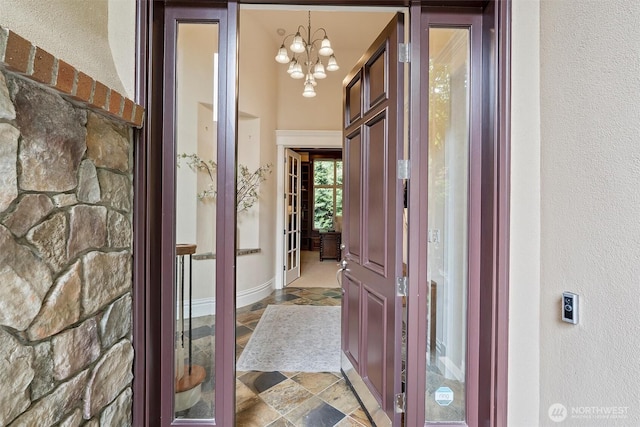 hallway featuring stone finish flooring, a textured wall, a chandelier, and baseboards