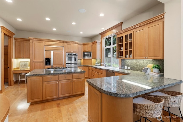 kitchen with built in appliances, a breakfast bar, a sink, light wood finished floors, and backsplash