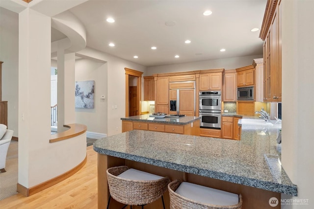 kitchen with a sink, built in appliances, recessed lighting, baseboards, and light wood-type flooring