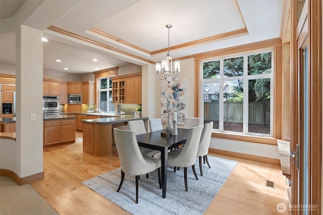 dining space with visible vents, baseboards, a raised ceiling, an inviting chandelier, and ornamental molding