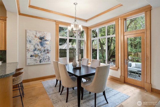 dining space featuring a tray ceiling, a chandelier, baseboards, and light wood finished floors