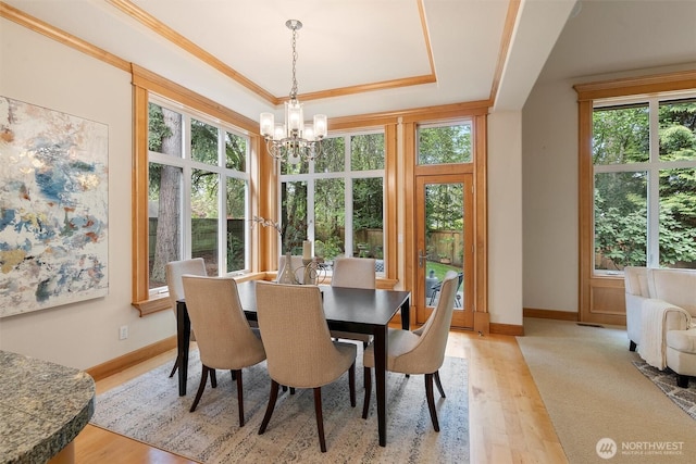 dining area with an inviting chandelier, baseboards, a tray ceiling, and light wood-style flooring