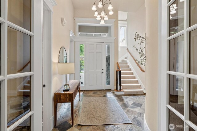 foyer featuring an inviting chandelier, baseboards, stairs, and a wealth of natural light
