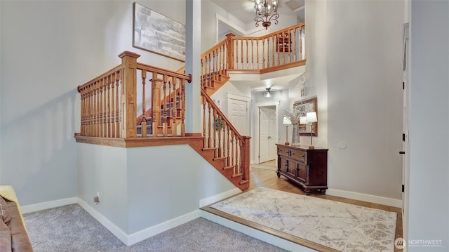 stairway featuring baseboards, a towering ceiling, and a notable chandelier