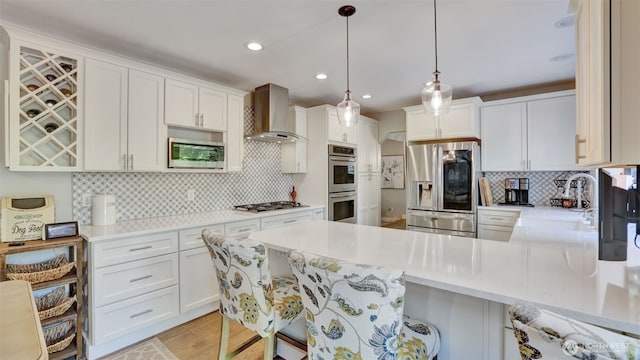kitchen featuring appliances with stainless steel finishes, tasteful backsplash, a sink, a peninsula, and wall chimney exhaust hood