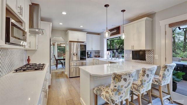 kitchen featuring ventilation hood, light wood-style flooring, stainless steel appliances, a peninsula, and tasteful backsplash