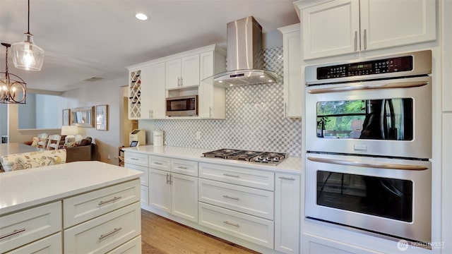 kitchen featuring wall chimney range hood, light countertops, decorative backsplash, and stainless steel appliances