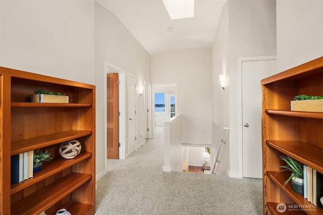 hall featuring carpet floors, baseboards, lofted ceiling with skylight, and an upstairs landing