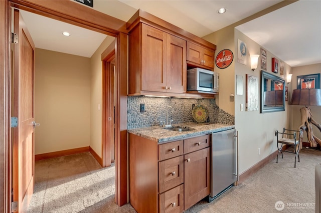 kitchen with fridge, stainless steel microwave, light colored carpet, a sink, and baseboards