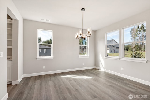 unfurnished dining area featuring a notable chandelier, visible vents, wood finished floors, and baseboards
