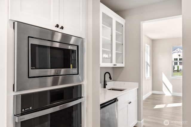 kitchen featuring white cabinets, glass insert cabinets, a sink, stainless steel appliances, and baseboards