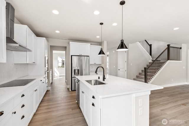 kitchen with light wood-style floors, appliances with stainless steel finishes, wall chimney range hood, backsplash, and a sink