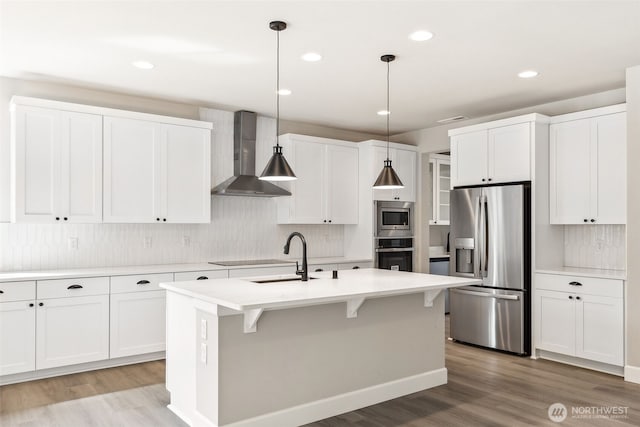 kitchen with decorative backsplash, a sink, appliances with stainless steel finishes, light wood-style floors, and wall chimney exhaust hood