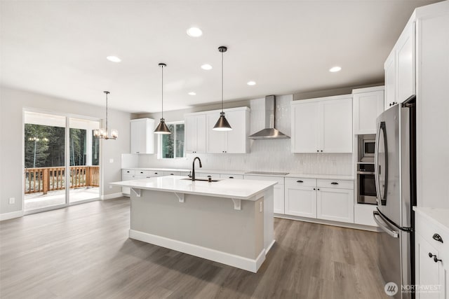 kitchen with stainless steel appliances, light countertops, a sink, light wood-type flooring, and wall chimney exhaust hood