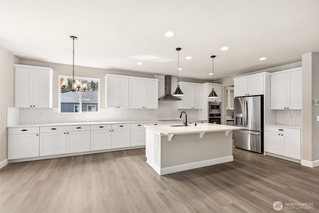 kitchen with tasteful backsplash, a sink, stainless steel appliances, light wood finished floors, and wall chimney exhaust hood