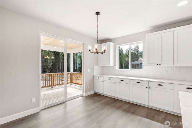 kitchen with white cabinetry, decorative backsplash, light wood-style flooring, light countertops, and an inviting chandelier