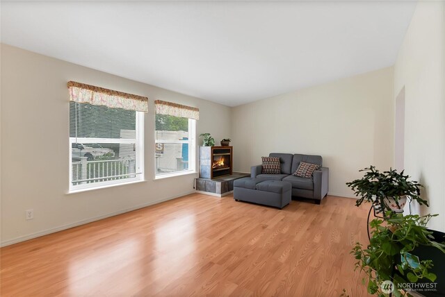 living area featuring a tiled fireplace, baseboards, and light wood finished floors