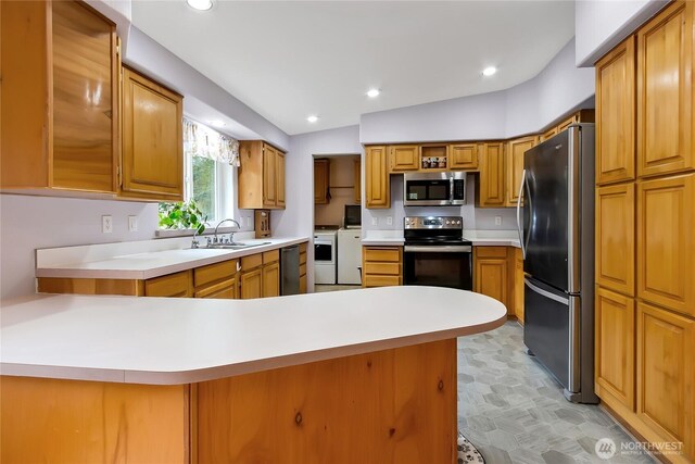 kitchen with washing machine and clothes dryer, a sink, light countertops, a peninsula, and stainless steel appliances