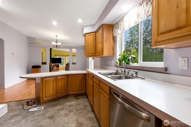 kitchen featuring stainless steel dishwasher, a peninsula, light countertops, a sink, and a notable chandelier