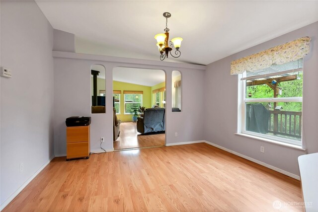 interior space with baseboards, an inviting chandelier, vaulted ceiling, and light wood finished floors