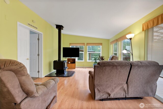 living room with visible vents, a wood stove, wood finished floors, and vaulted ceiling